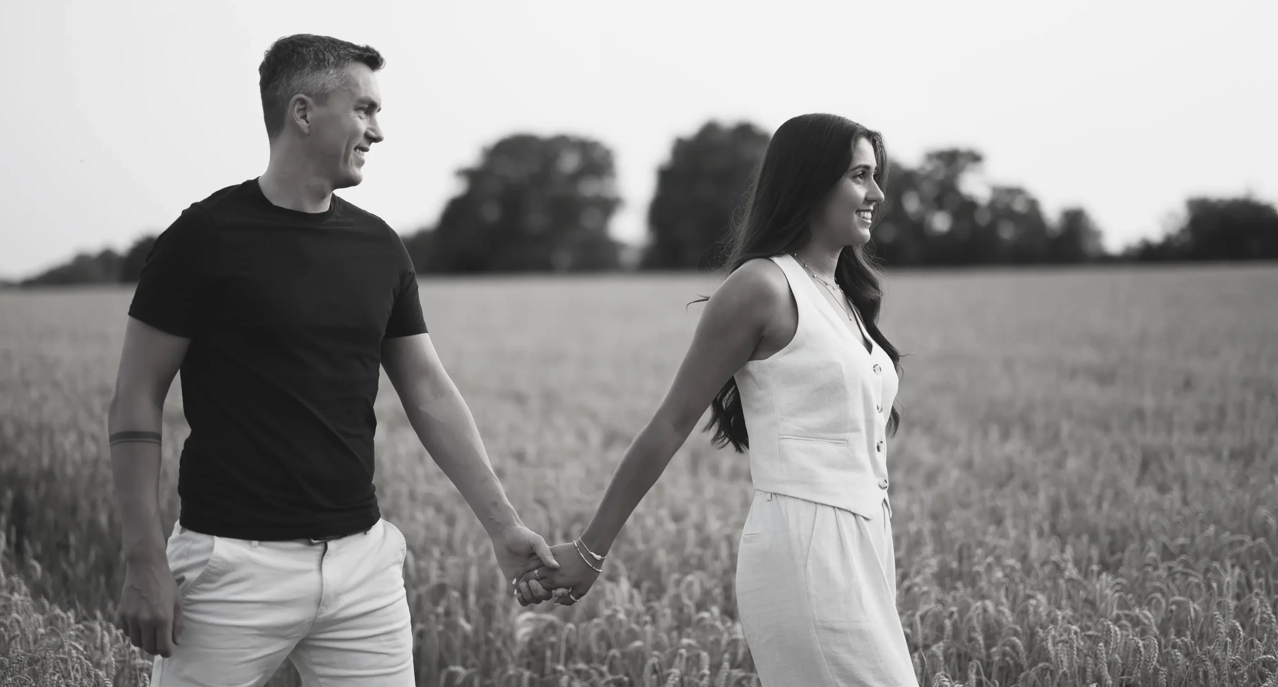 Black and white wedding photography of couple walking through field