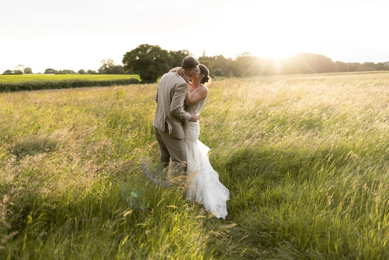 Wedding photography of bride and groom kissing in sunlit meadow