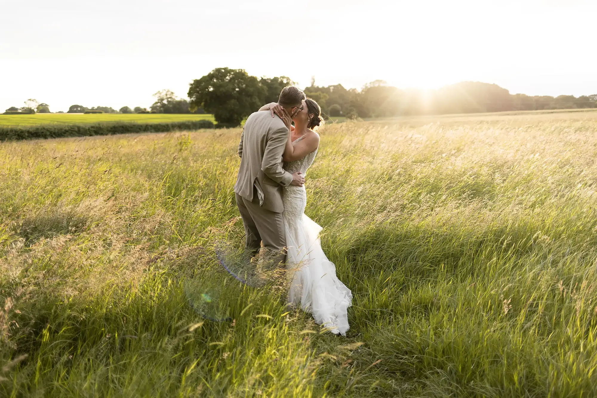 Wedding photography of bride and groom kissing in a meadow at sunset